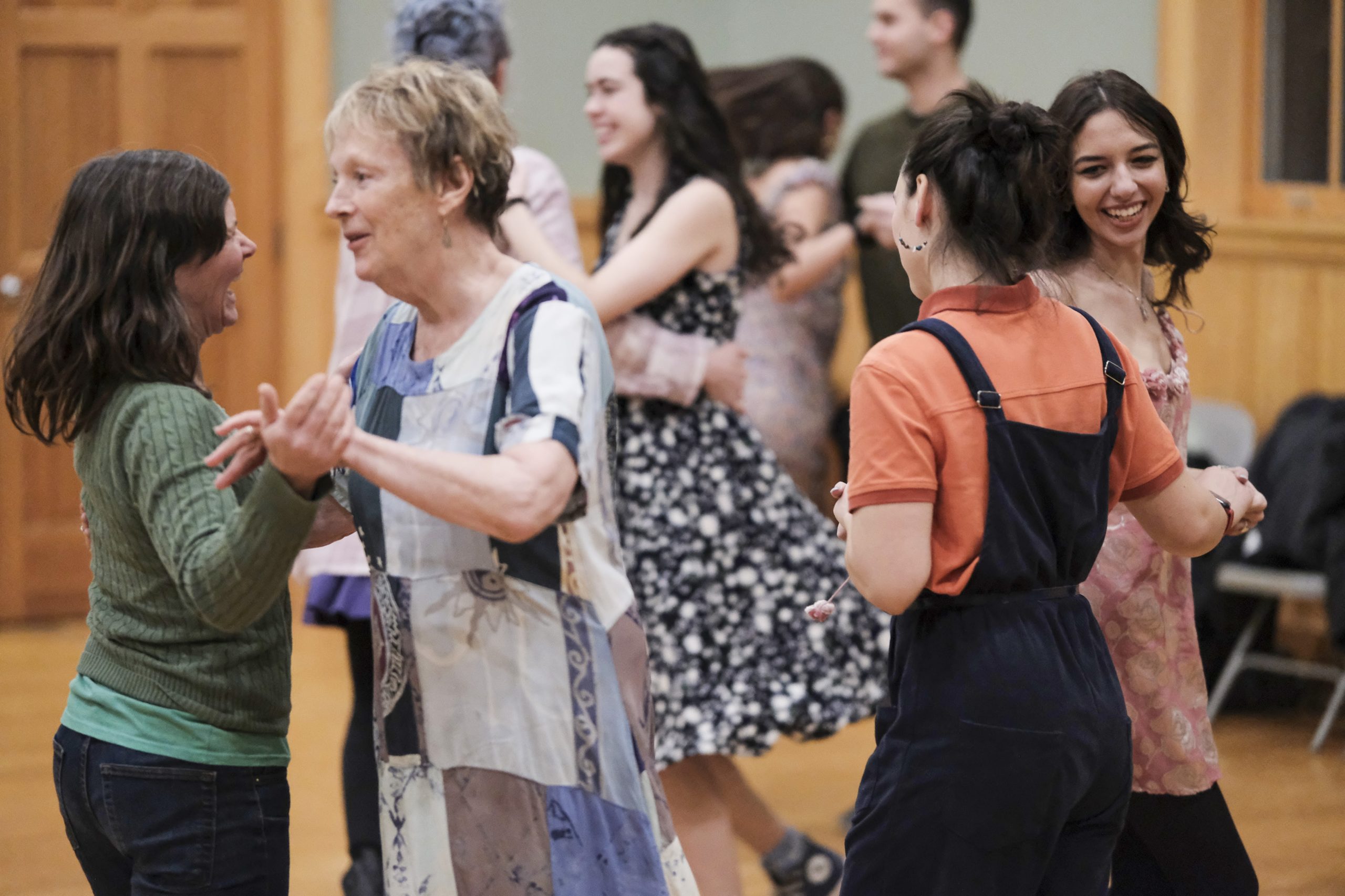 A group of people of different ages and genders dance in pairs, smiling.